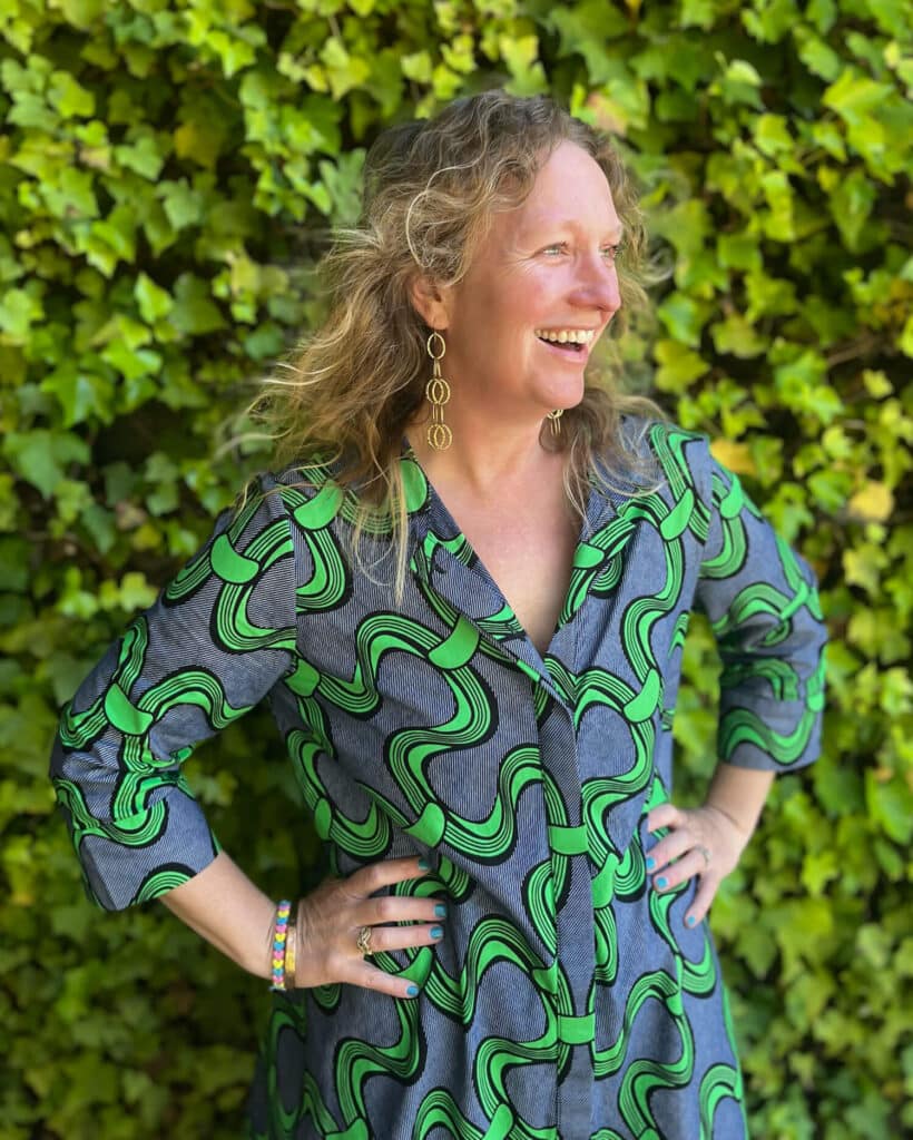 Heather Lazare, Independent Editor and cofounder of Northern California Writers Retreat, stands in front of a vine-covered wall and smiles with her hands on her hips